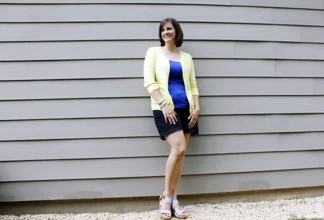 Solid colors make and easy Disneybound outfit as shown by a woman wearning a blue tank top, yellow cardigan, and black shorts.