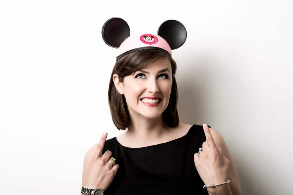 Woman pointing and looking up at her pink hat with Mickey Mouse ears