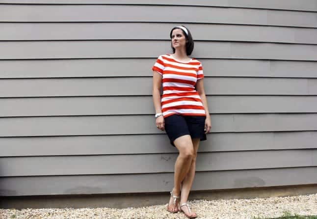 Woman with orange striped shirt standing against a wall.