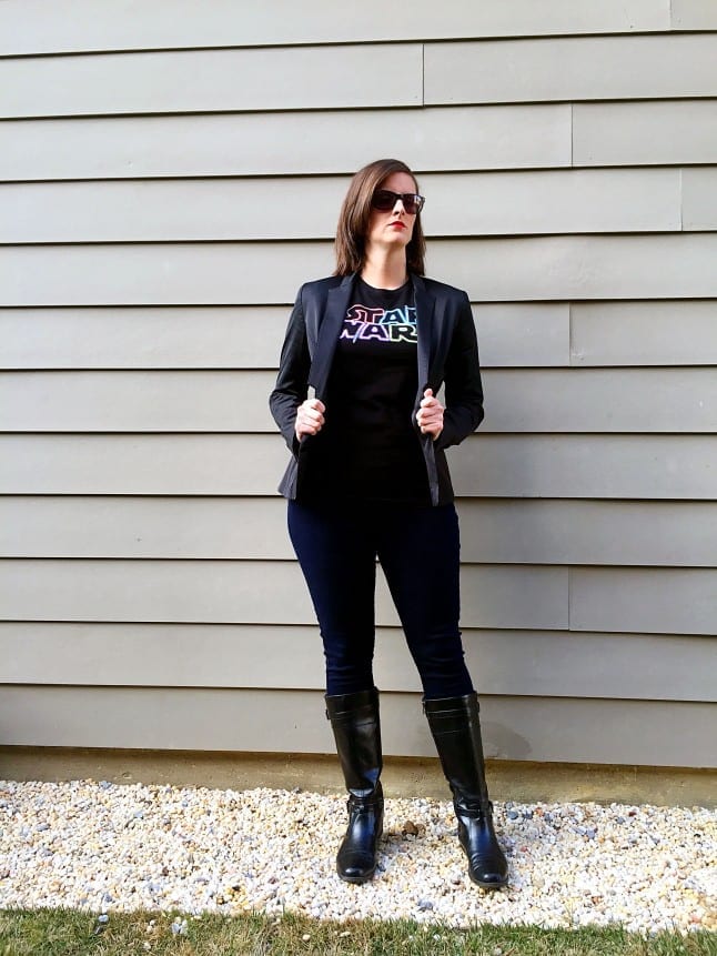 Woman posing with all-black outfit with Star Wars logo on shirt and black boots.