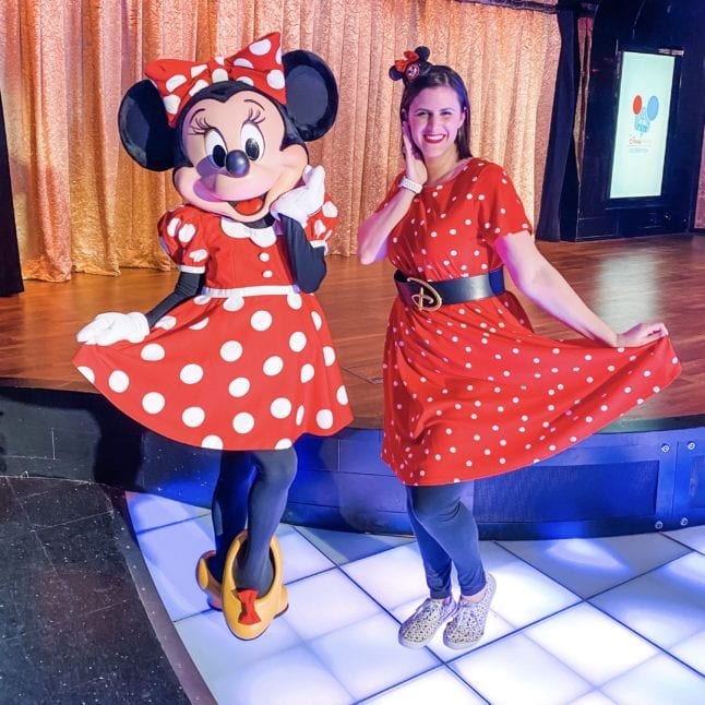 Woman in red, polka dot dress posing with Minnie Mouse.