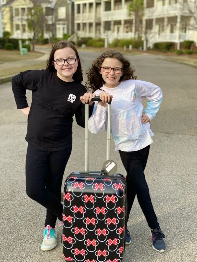 Two girls pose with Minnie Mouse suitcase